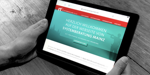Bild der neuen Website der Systemberatung Mainz auf einem Tabel, das von zwei Händen gehalten wird.